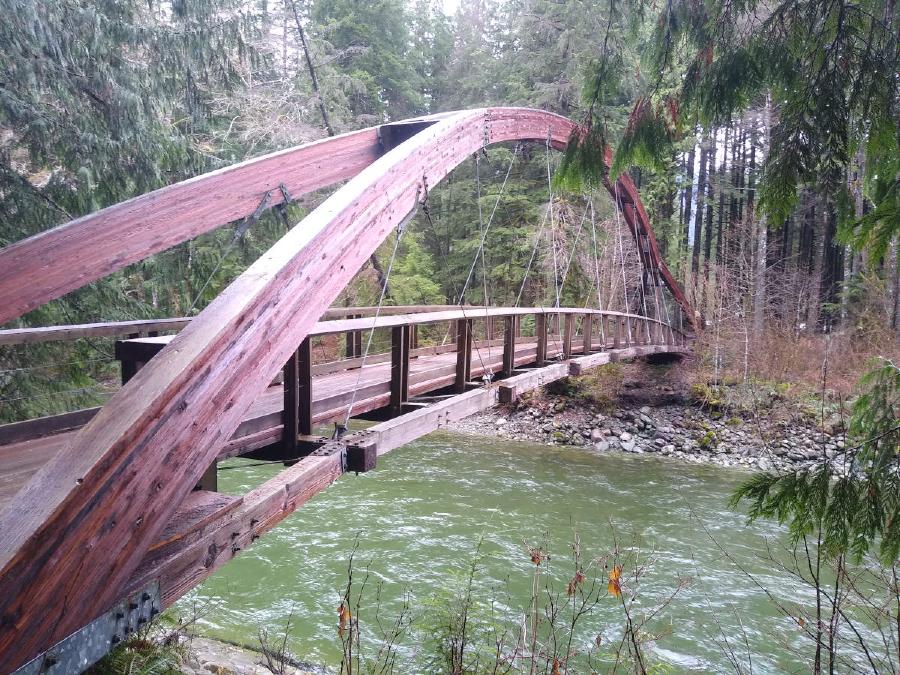 An arched wooden bridge, with wooden decking beneath suspended on taught metal cables.