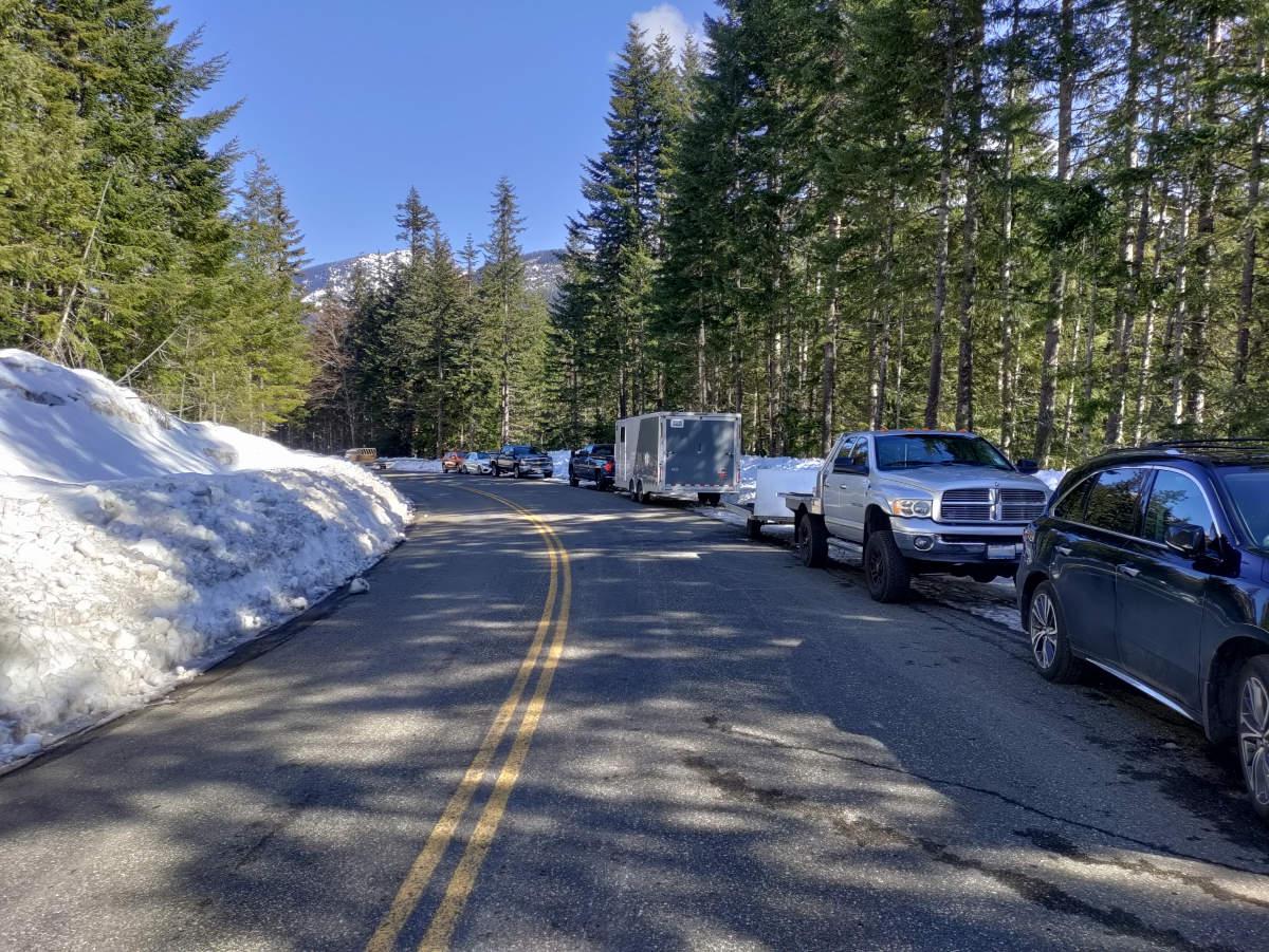 A clear road, with a steep bank of snow on the left, and cars parked all along the right.