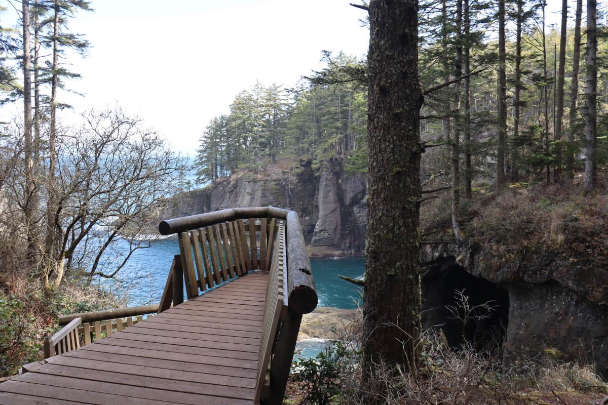 A wooden viewing platform the leans out towards the cliff edge, with a drop down to the sea, and cliffs around to the right.