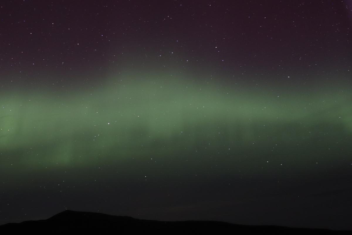 Photo of green aurora over mountains.