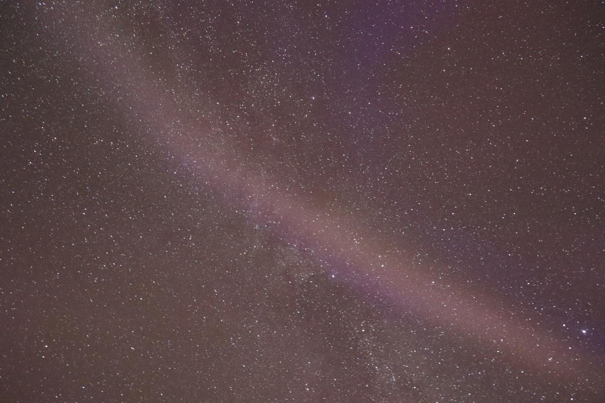 Photo looking straight up at stars with the aurora as a faint diagonal white line.