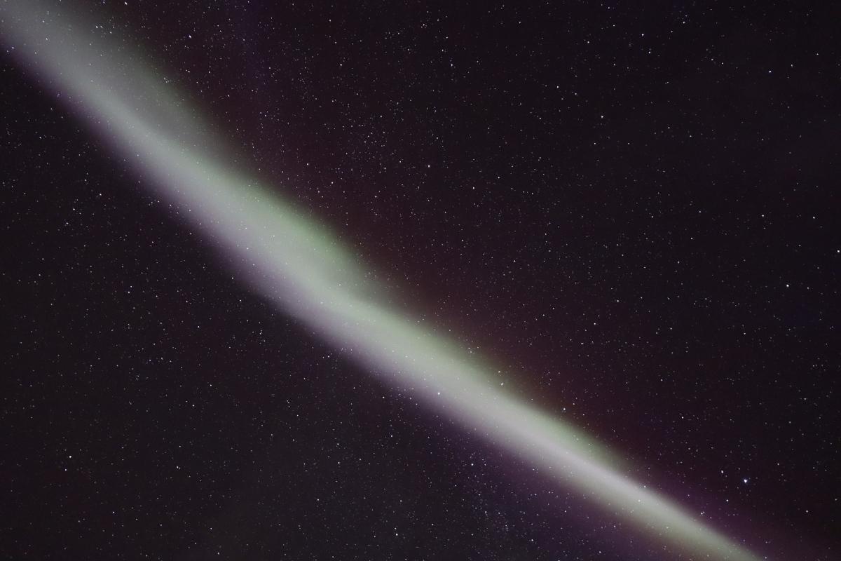 Photo looking straight up at stars with the aurora as a bright diagonal white line.