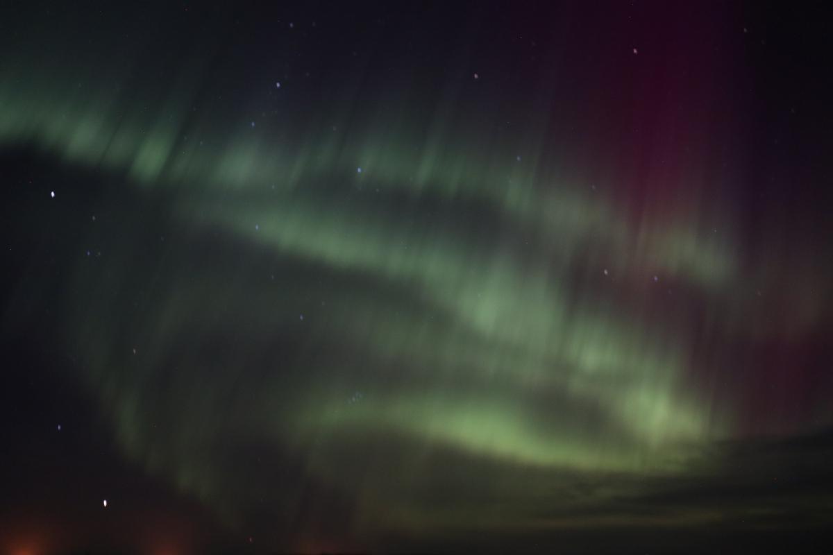 Photo of green 'S' shaped aurora over mountains.