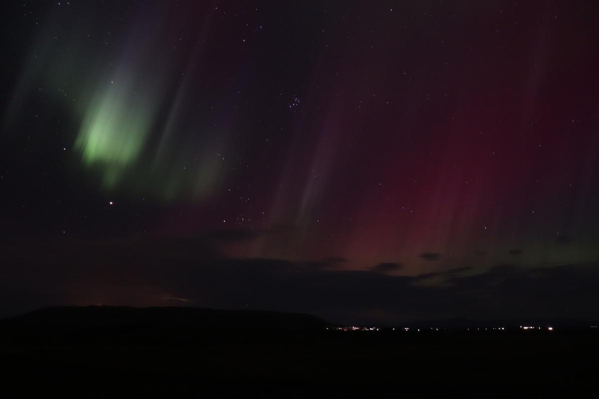 Photo of bright green and red aurora over lights.