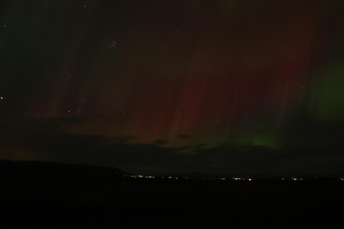 Photo of faint green and red aurora over lights.