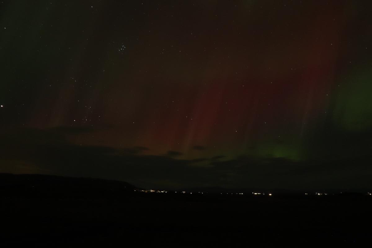 Photo of faint green and red aurora over lights.
