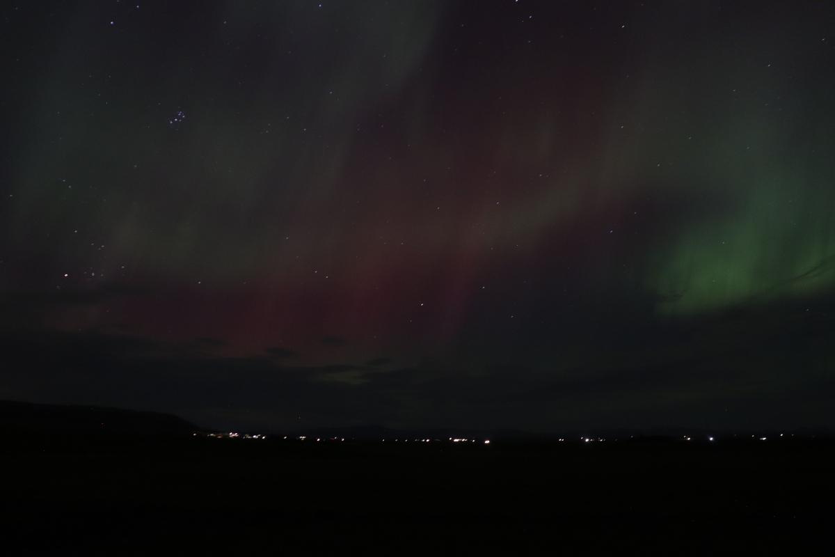 Photo of faint green and red aurora over lights.