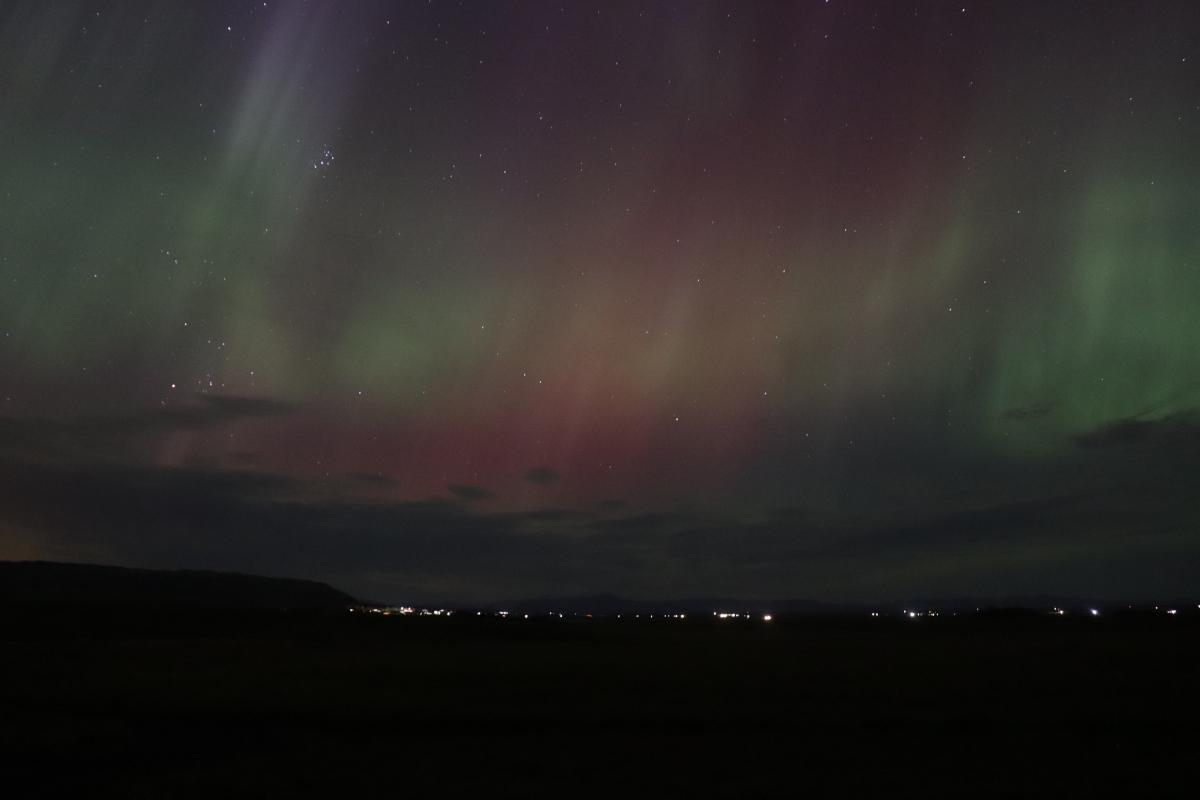 Photo of faint green and red aurora over lights.