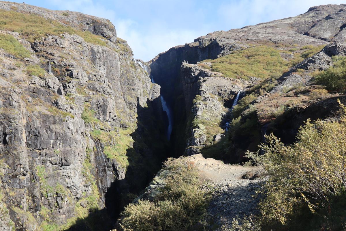 Photo looking into a canyon cast in shadows, with a 200m waterfall hiding in the back.