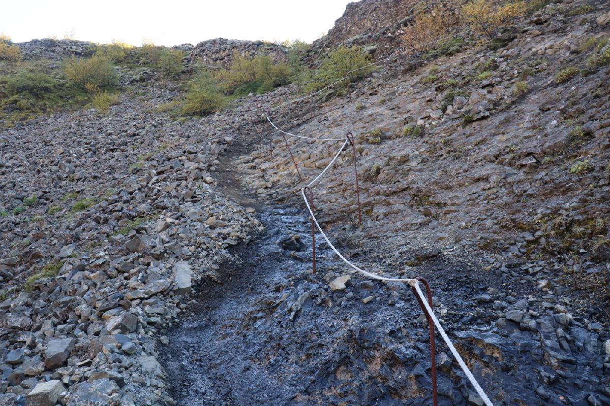 Photo of a steeply descending, rocky path, partly wet, with some poles and rope for handrail.