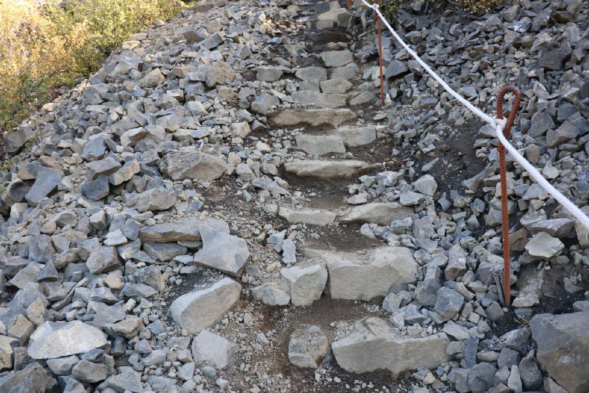 Photo of scree with large, stable stones placed for steps, and a vertical metal poles connecting with ropes for a handrail.