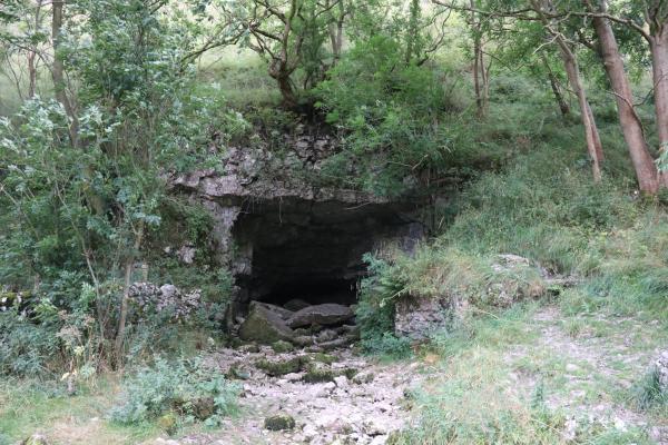 A rocky entrance into a dark cave, set into the side of a green valley.