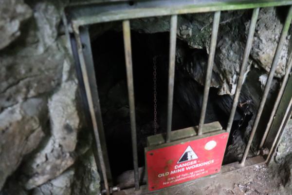 Looking through the cage into the darkness. A chain is dangling, vanishing into the black below.