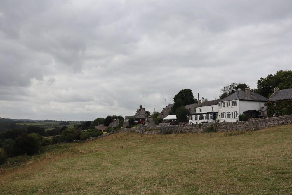 A gentle hillside with a stone wall at the top, and behind that, a white pub.