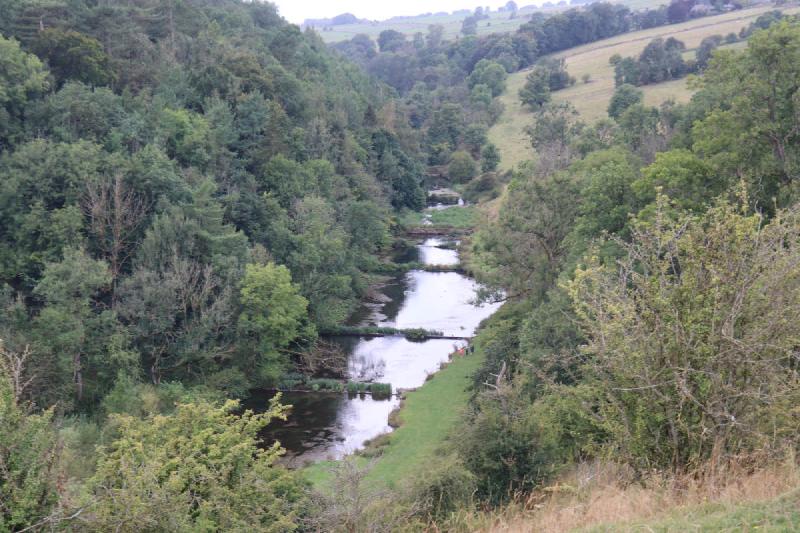 Looking down on a river in a valley. The river is calm with a series of small weirs.