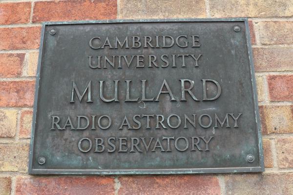 A brick wall with metal plaque with the text 'CAMBRIDGE UNIVERSITY MULLARD RADIO ASTRONOMY OBSERVATORY'.