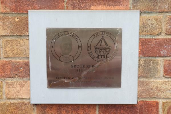 A brick wall with metal plaque with the text 'GROTE REBER (1911 - 2002) ELECTRICAL ENGINEER AND PIONEER ASTRONOMER'.