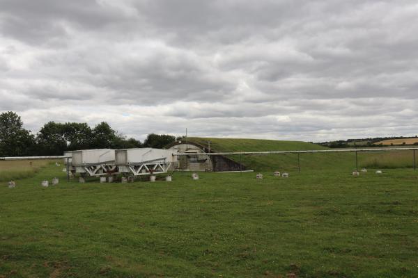 A bunker covered in grass, with some white boxes and pipes on the field outside.