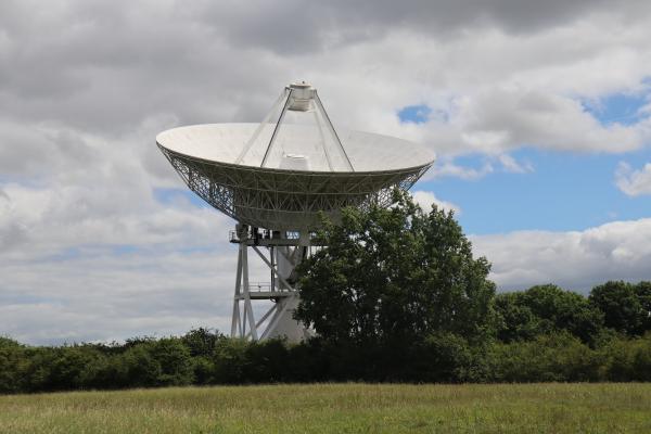 A big parabolic receiver on a tower behind a line of trees.