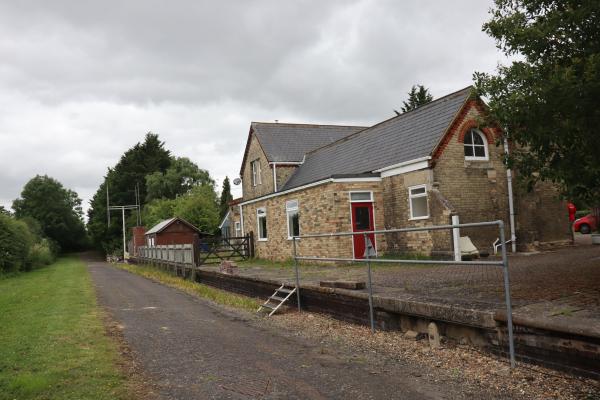 An old station platform, with no railway track, and the old railway station building in the background.
