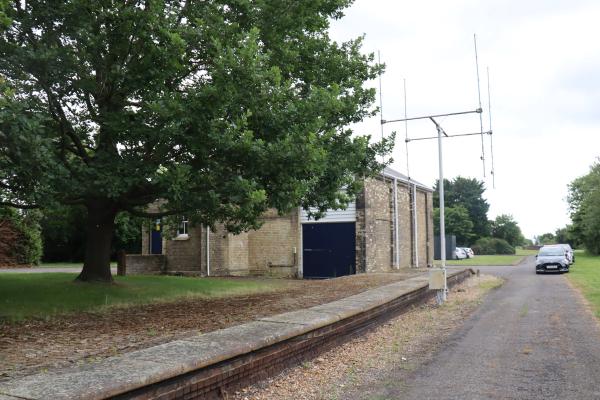 An old station platform, with no railway track, and an antenna and the old goods shed is in the background.
