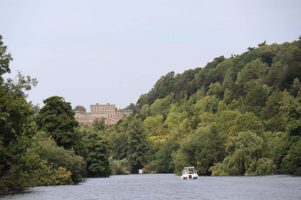 A country house on the hill in the distance overlooking the river, with wooded hillside to the right.