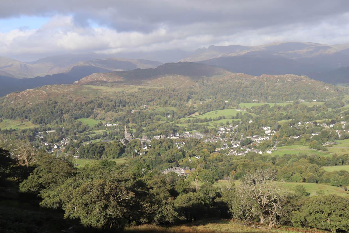 Looking down on the whole of Ambleside, with a church tower, scattered buildings and numerous trees down in the valley below.