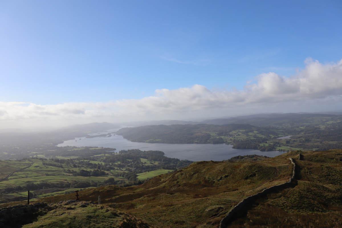 A distant view of Windermere, with blue sky overhead, but grey clouds in the distance.