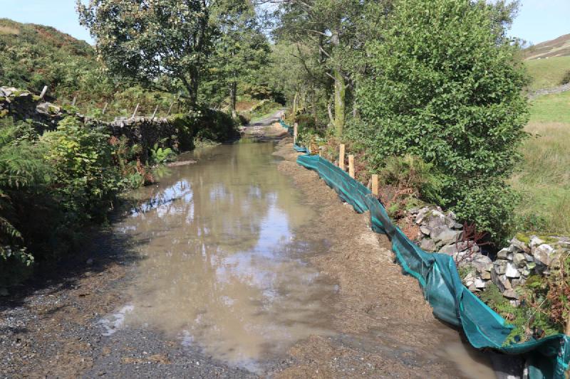 A submerged gravel road with a line of hay piles on the side.