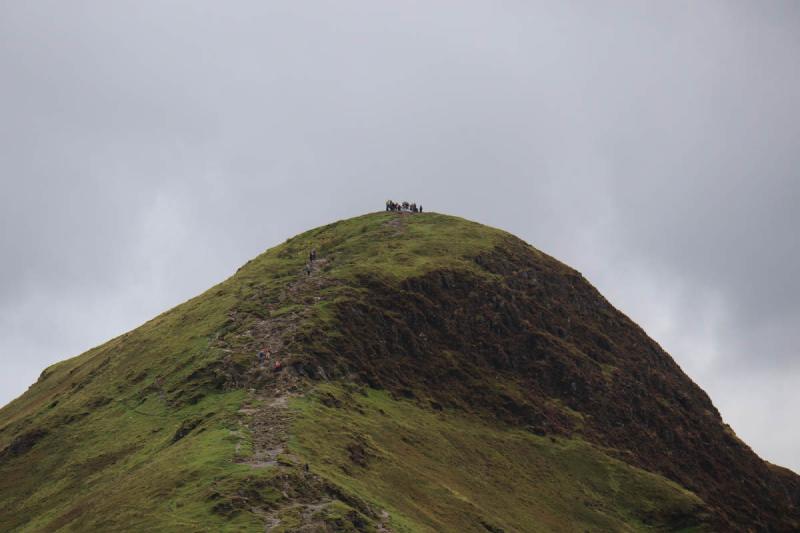 A group of people huddled on the top of a distant summit.