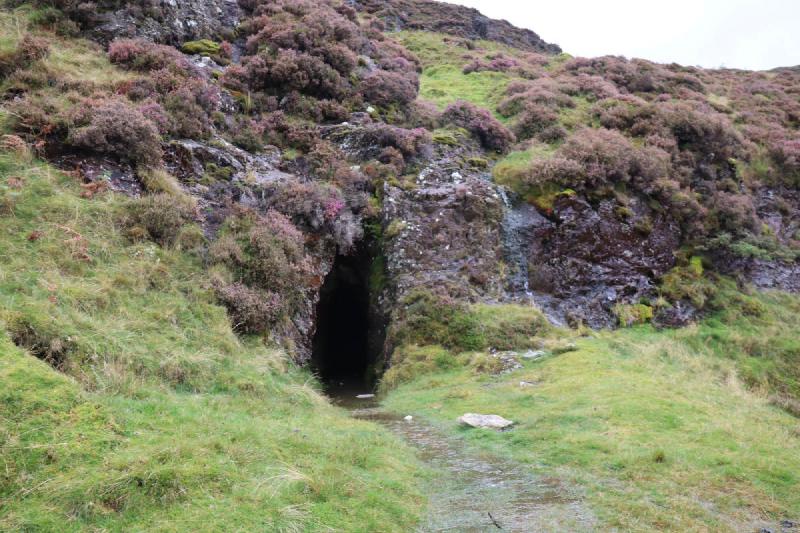 A cave entrance about the size of a person, with a stream of water coming out.